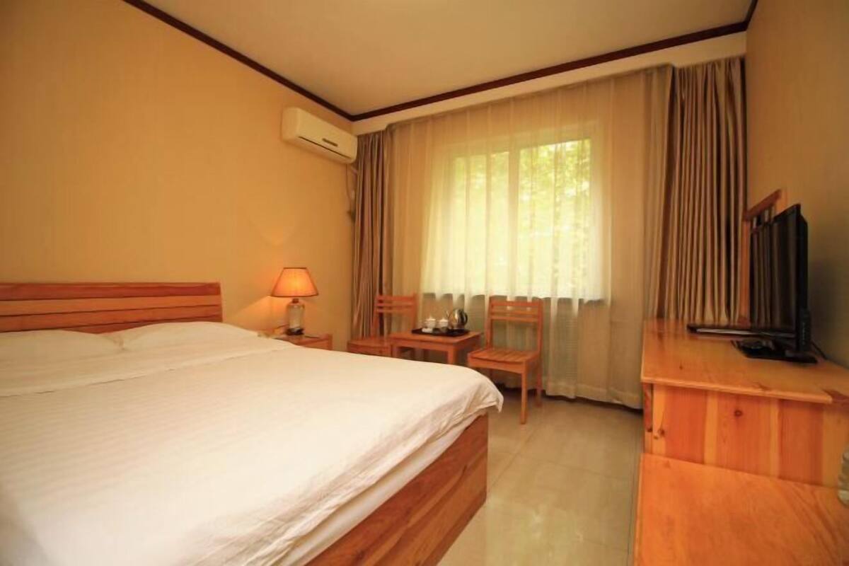 A hotel room with a bed, a desk, a chair, a television, and a window with curtains.
