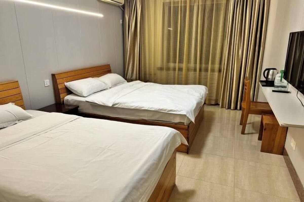 A hotel room with two single beds, a wooden desk, a television, and a window with curtains.