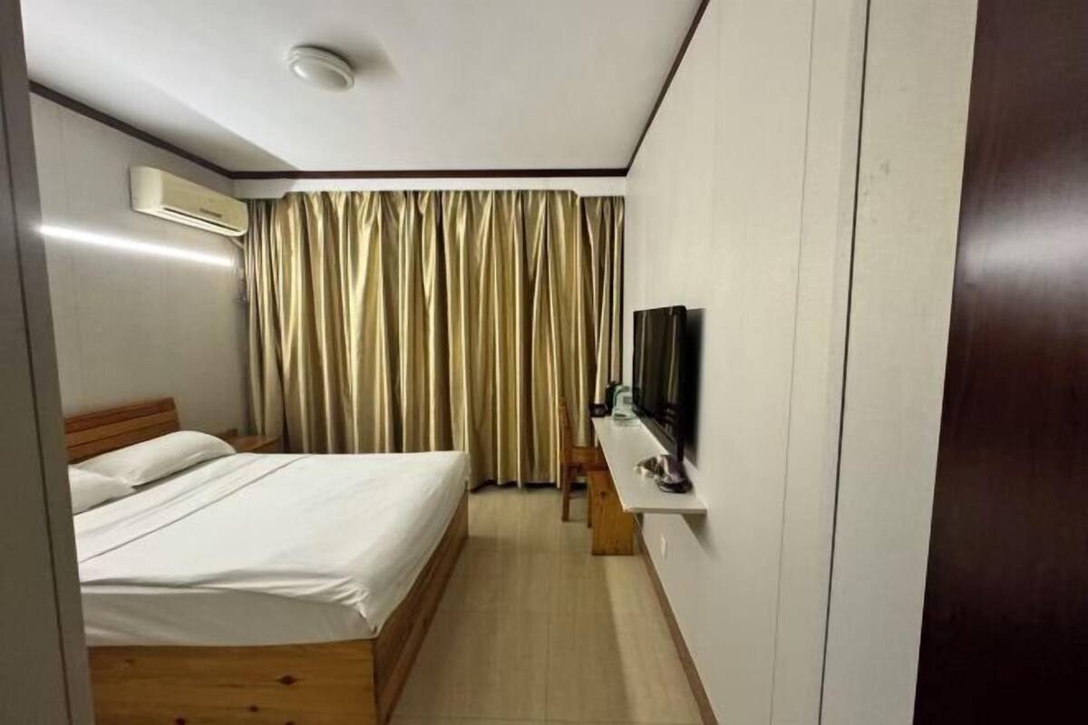 A bedroom with a bed, an air conditioning unit, a television on a stand, and a curtain.