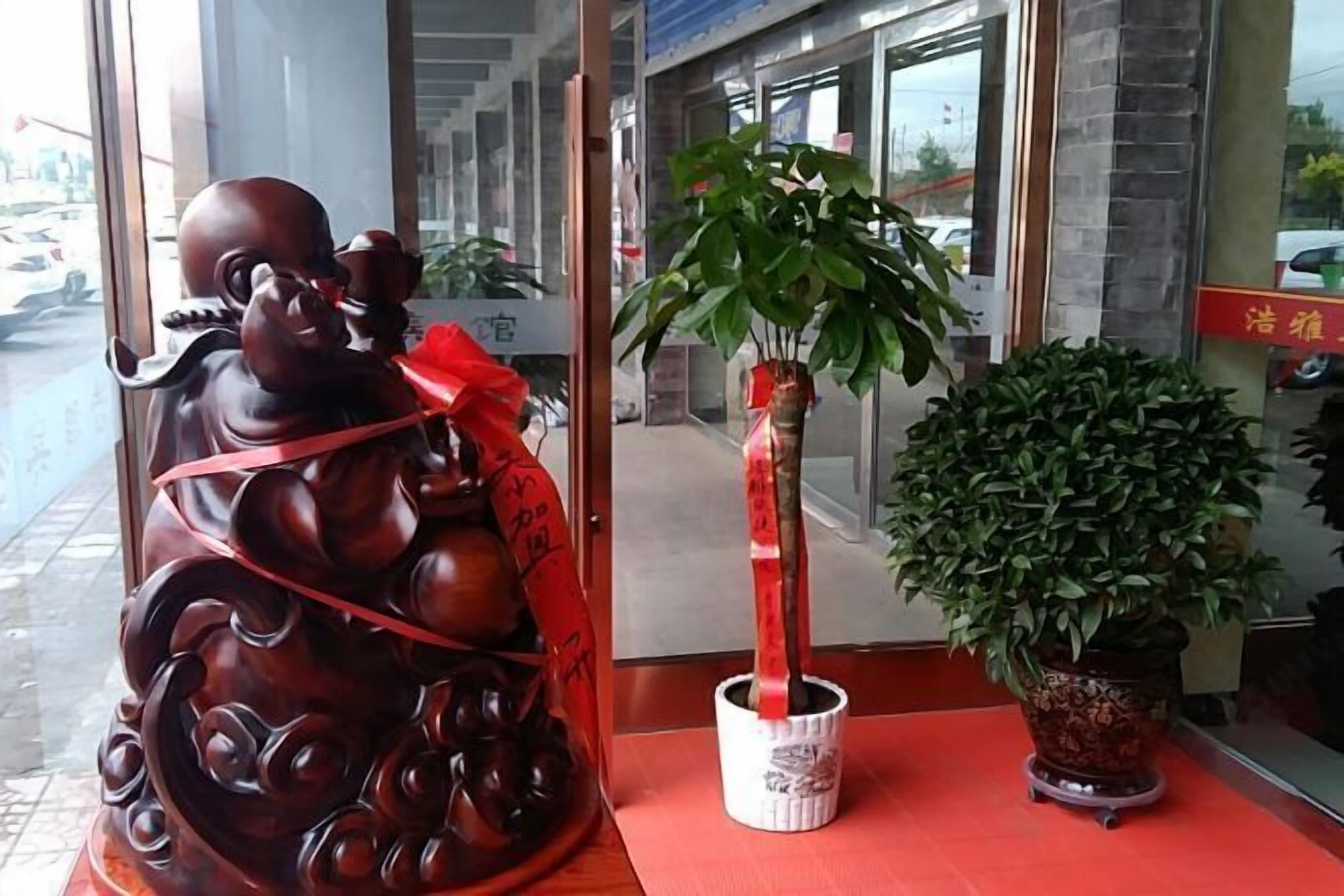 Eine Statue mit rotem Band, ein Blumentopf und eine große Zimmerpflanze in einer Hotelhalle.