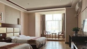 Ein Hotelzimmer mit zwei Betten, einem Schreibtisch, einem Stuhl, einem Fernseher und einem großen Fenster mit Vorhängen.