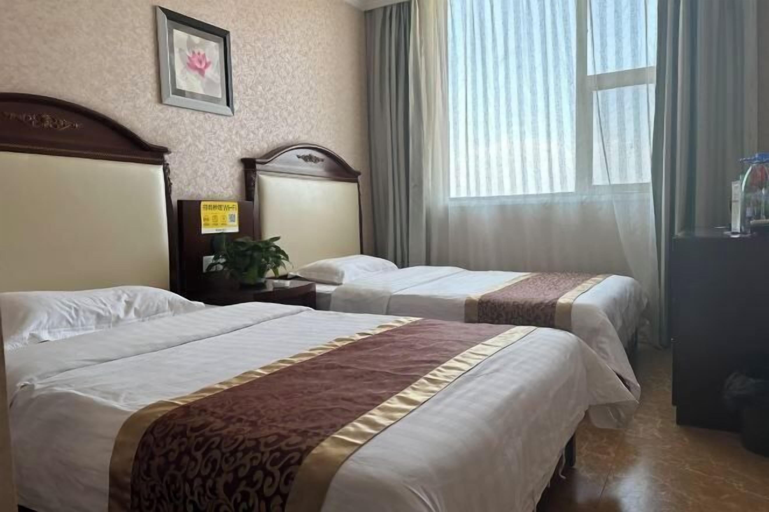 Habitación de hotel con dos camas, cabecero de madera, mesita de noche con lámpara, un cuadro enmarcado en la pared y una ventana con cortinas.