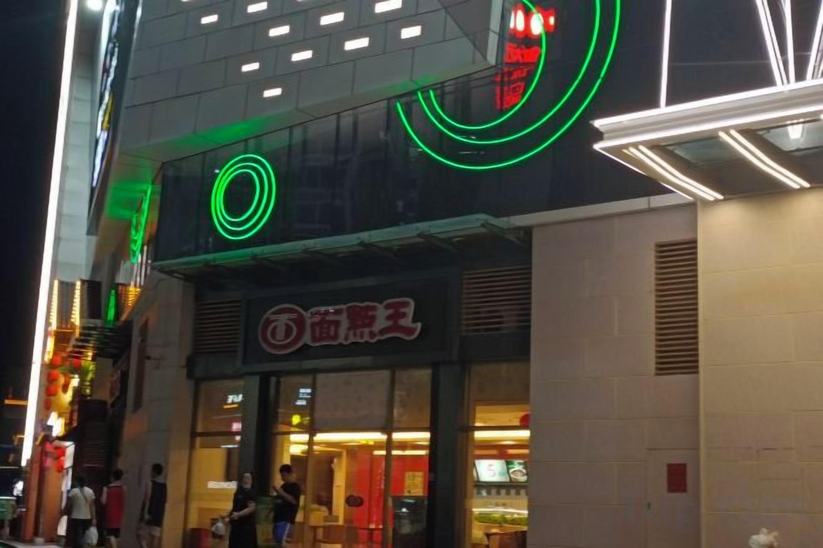 A building with a storefront featuring a neon sign and a visible entrance.