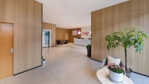 A modern hotel lobby with wooden panel walls, a reception desk, and a dining area in the background. - Shankee Hotel (Shenzhen International Exhibition Center Haoxiang Subway Station) (Shenzhen)