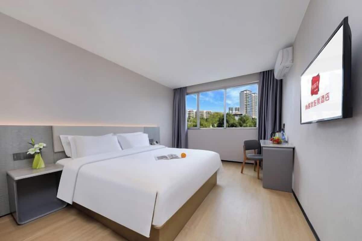 A modern hotel room with a large bed, a desk, and a TV mounted on the wall.