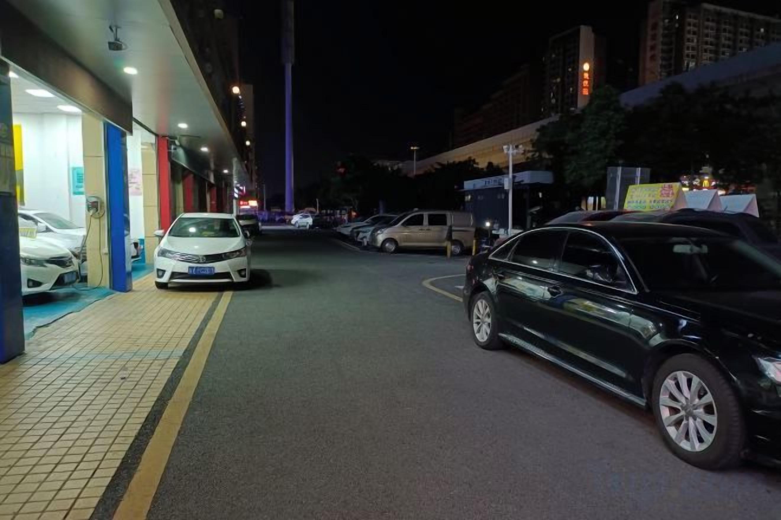 A nighttime parking area with cars parked along the side of a building.