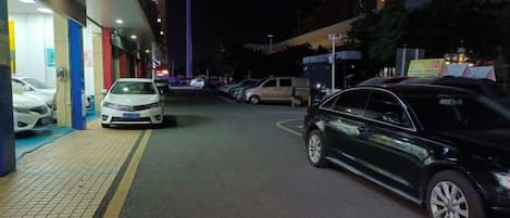 A nighttime parking area with cars parked along the side of a building.