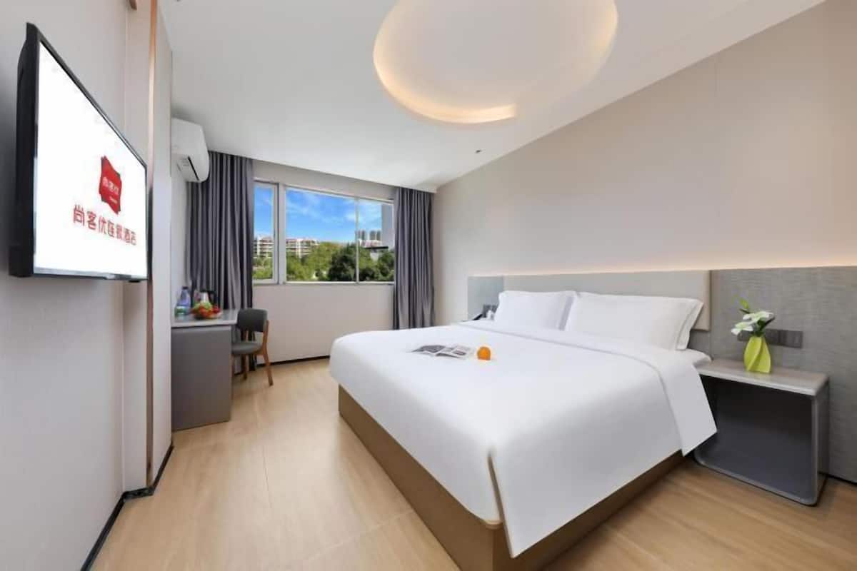 A modern hotel room with a large bed, a desk, and a TV.