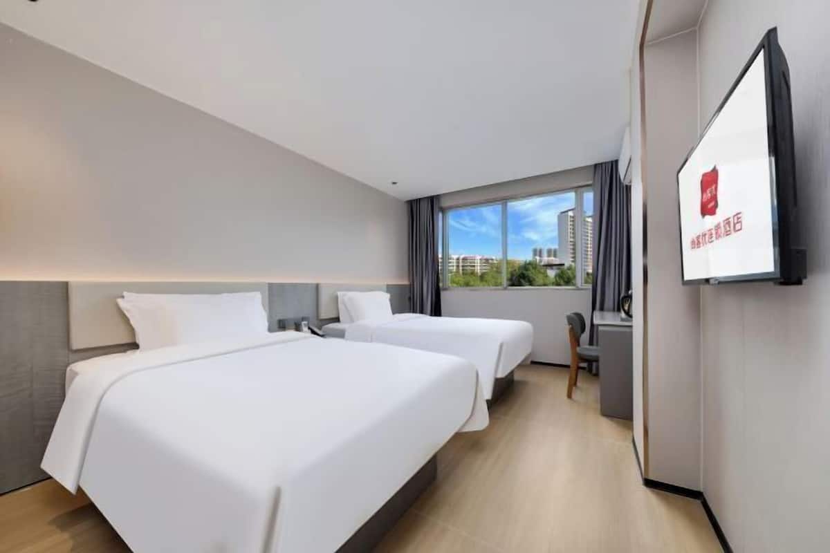A hotel room with two beds, a desk, a chair, and a TV on the wall.