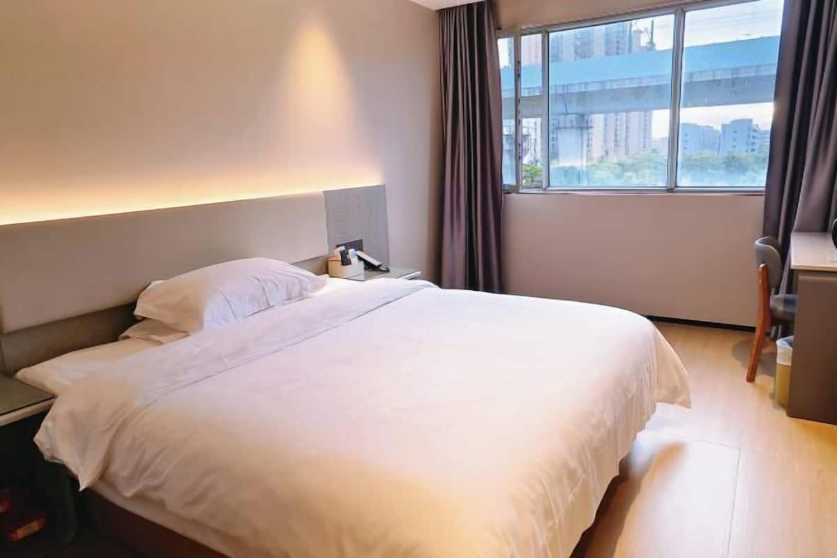 A hotel room with a large bed, a desk, and a view of buildings through the window.