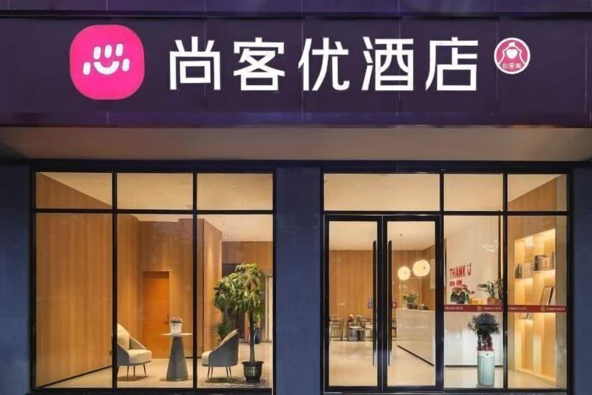 A hotel entrance with a modern design, featuring glass doors and a reception area visible through the windows.