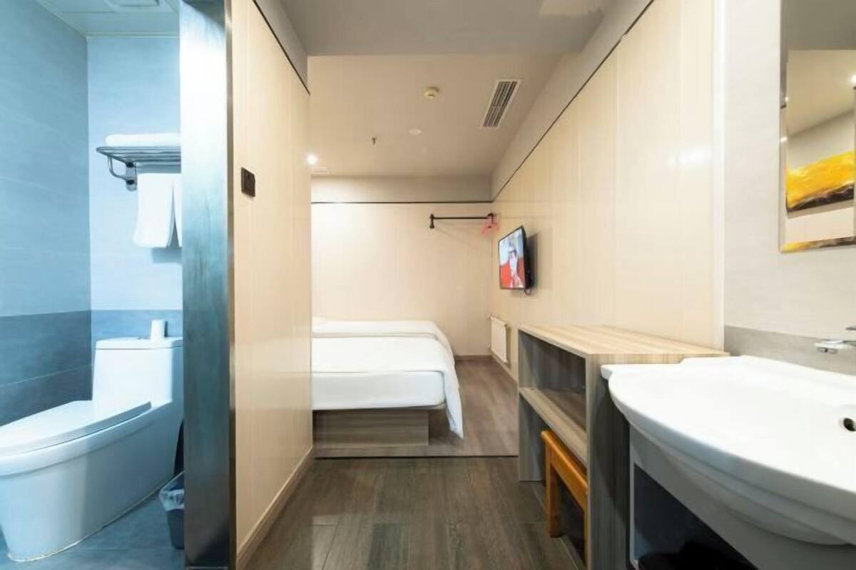 Une chambre d’hôtel équipée d’une douche, d’un lit, d’un lavabo et d’un téléviseur fixé au mur.