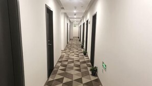Ein langer Korridor mit Schachbrettfußboden, Türen an beiden Seiten und Blumentöpfen entlang der Wände.
