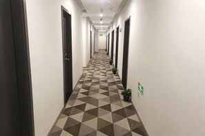 Pitkä käytävä, jossa on ruutukuvioinen lattia, ovet molemmin puolin ja ruukuissa olevia kasveja seinien varrella.