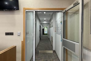 A corridor with a glass door on the left, a television mounted on the wall, and a poster on the right wall. - Homeinn Pebble Hotel (Beijing Tongren Hospital Chongwenmen Subway Station) (Beijing)