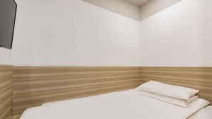 Camera d'angolo con un letto imbottito in legno, copripiumino bianco e televisore a schermo piatto montato a parete.