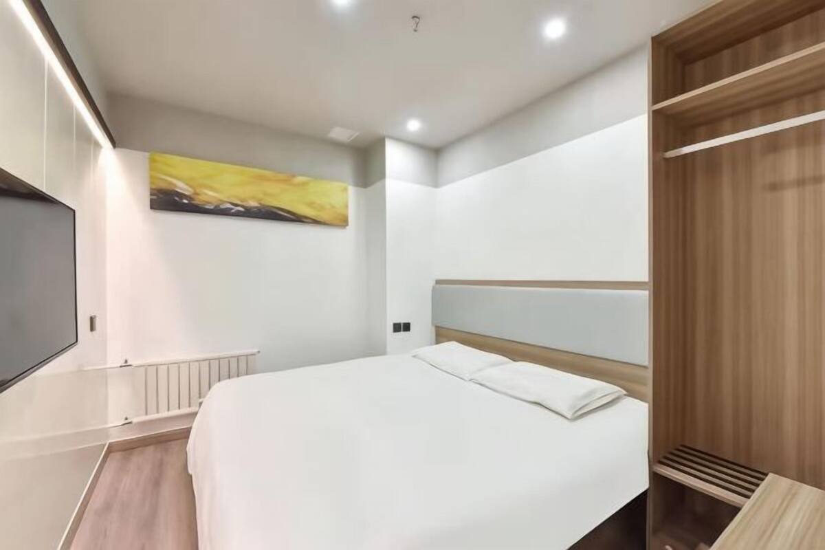 Une chambre d’hôtel moderne avec un grand lit, un téléviseur à écran plat, une armoire en bois et un tableau au mur.