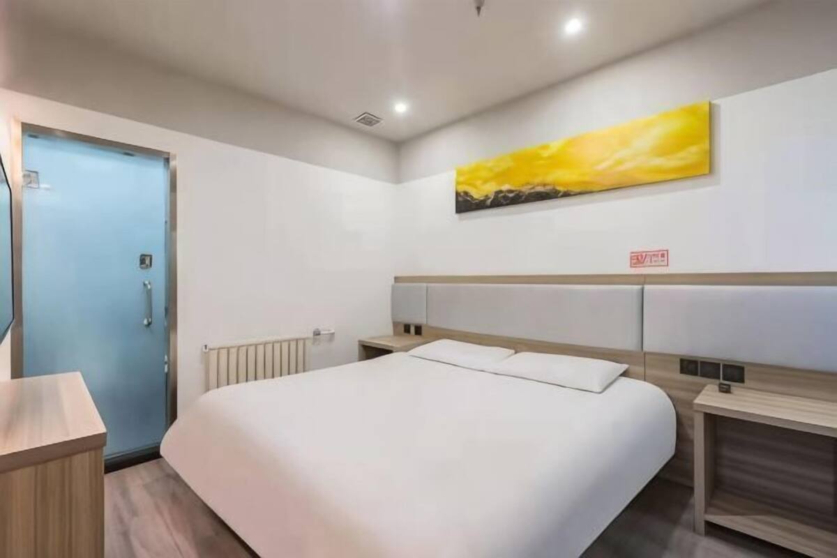 Une chambre d’hôtel avec un lit, des tables de chevet, un radiateur, une porte bleue et un tableau au mur.
