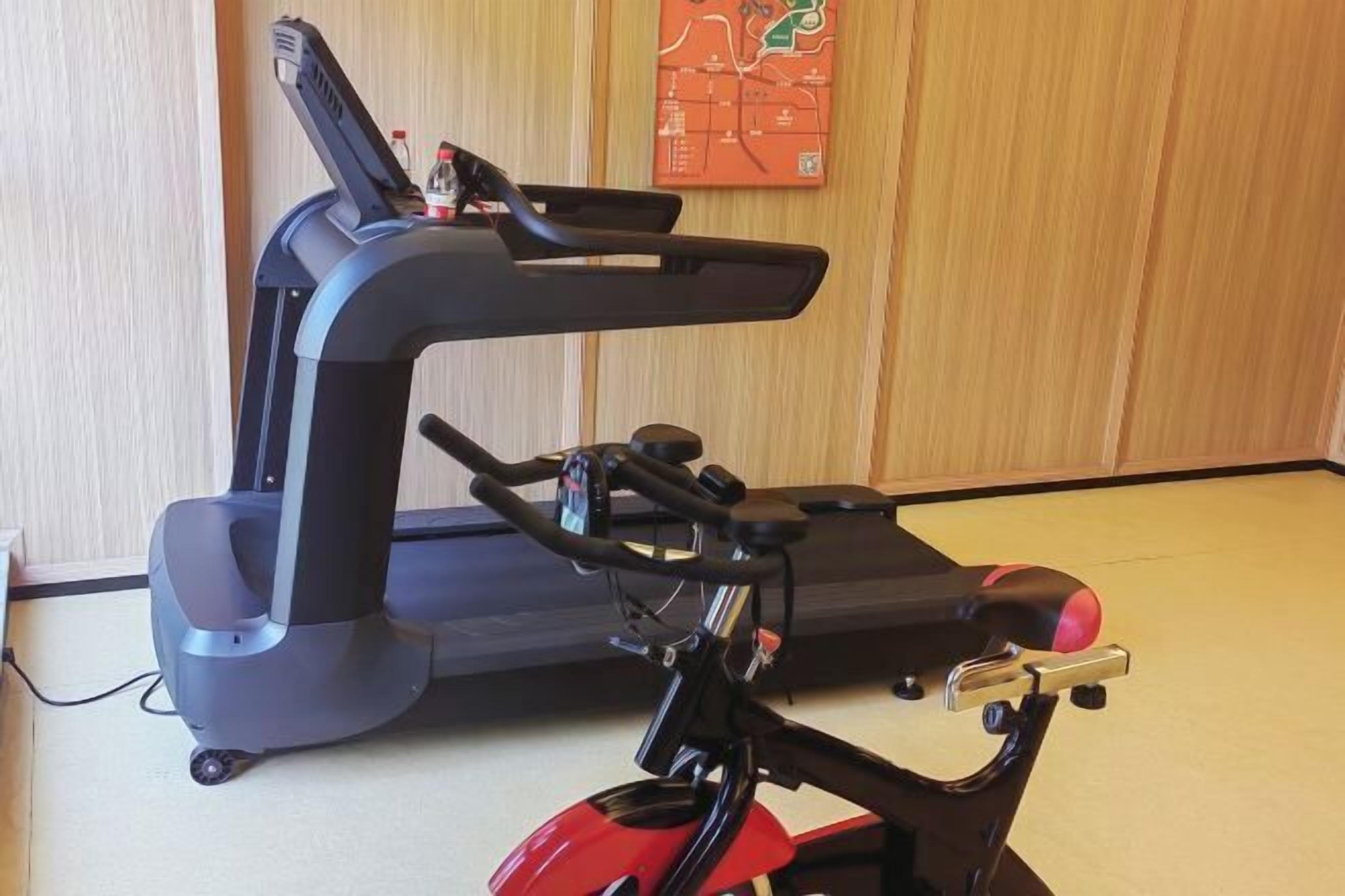 Un vélo d’appartement doté d’un écran numérique et d’une selle rouge, placé dans une pièce aux murs recouverts de lambris en bois et ornée d’une carte.