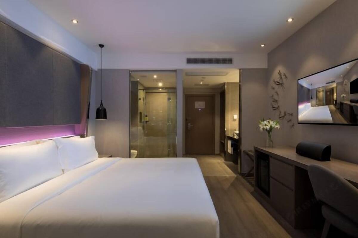 A modern hotel room with a large bed, a desk, and a mirror.