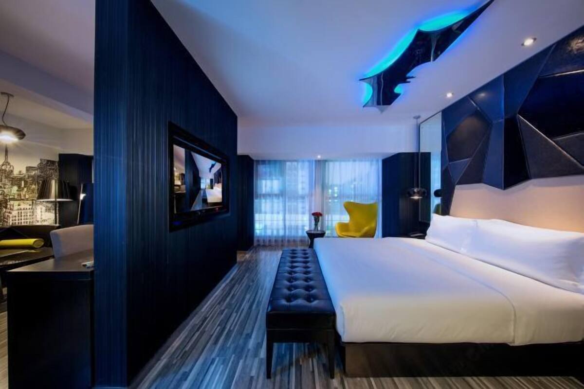 A modern hotel room with a large bed, a television, a desk, and a chair.
