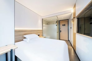 A modern hotel room with a large bed, a bedside table, a mirror, and a view of the hallway. - Qingji Hotel MINI (Shanghai Overseas Gaoqiao Guangming Road Branch) (Shanghai)