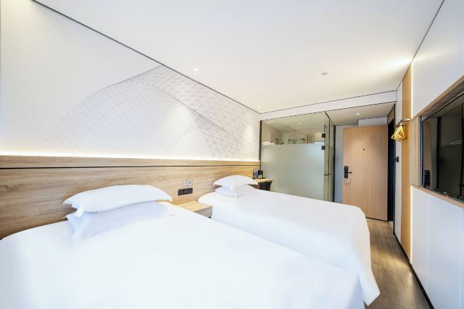 Habitación de hotel con dos camas, cabecera de madera, un espejo grande y vista al pasillo.