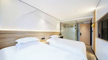 Habitación de hotel con dos camas, cabecera de madera, un espejo grande y vista al pasillo.
