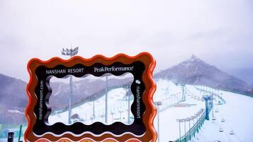 Une enseigne avec les inscriptions « Nanshan Resort » et « PeakPerformance », un paysage de montagne enneigé en arrière-plan et un télésiège.