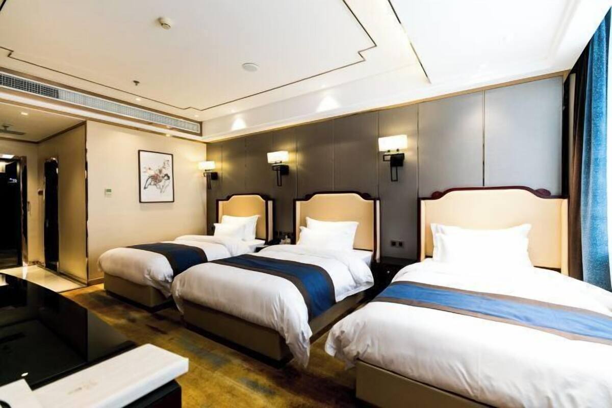 A hotel room with three beds arranged in a row, a desk, and a large window with curtains.