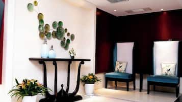 A reception area with a black console table, two chairs with floral cushions, and potted plants.