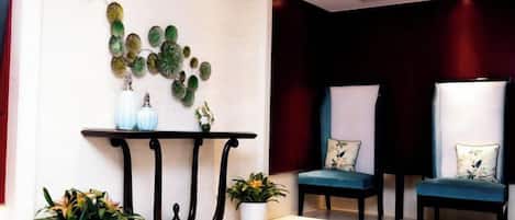 A reception area with a black console table, two chairs with floral cushions, and potted plants.