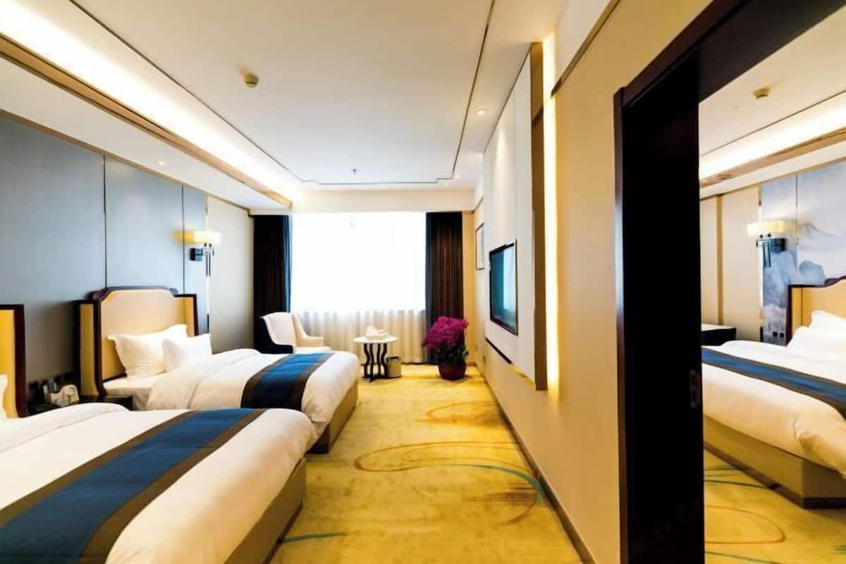 A hotel room with two beds, a small table, a chair, a potted plant, and a large mirror.