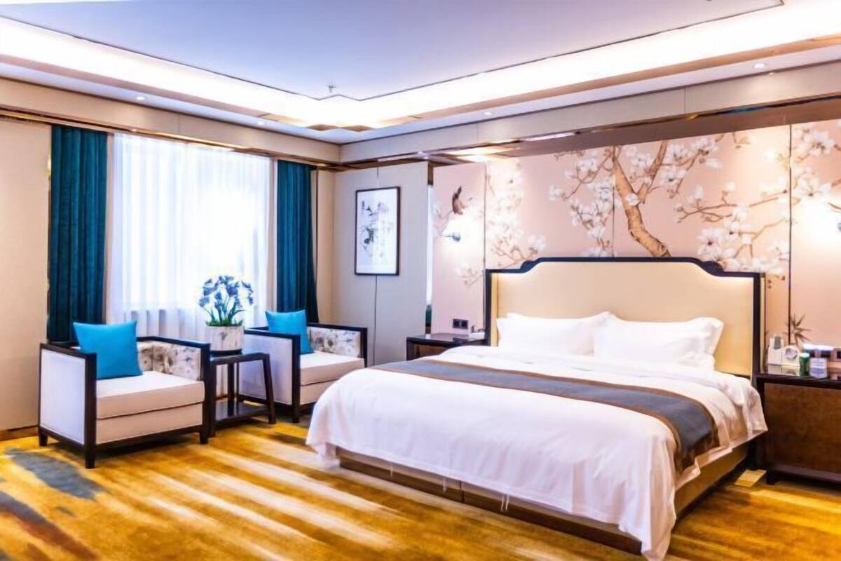 A hotel room with a large bed, a sofa, a nightstand, and a wall with a floral design.