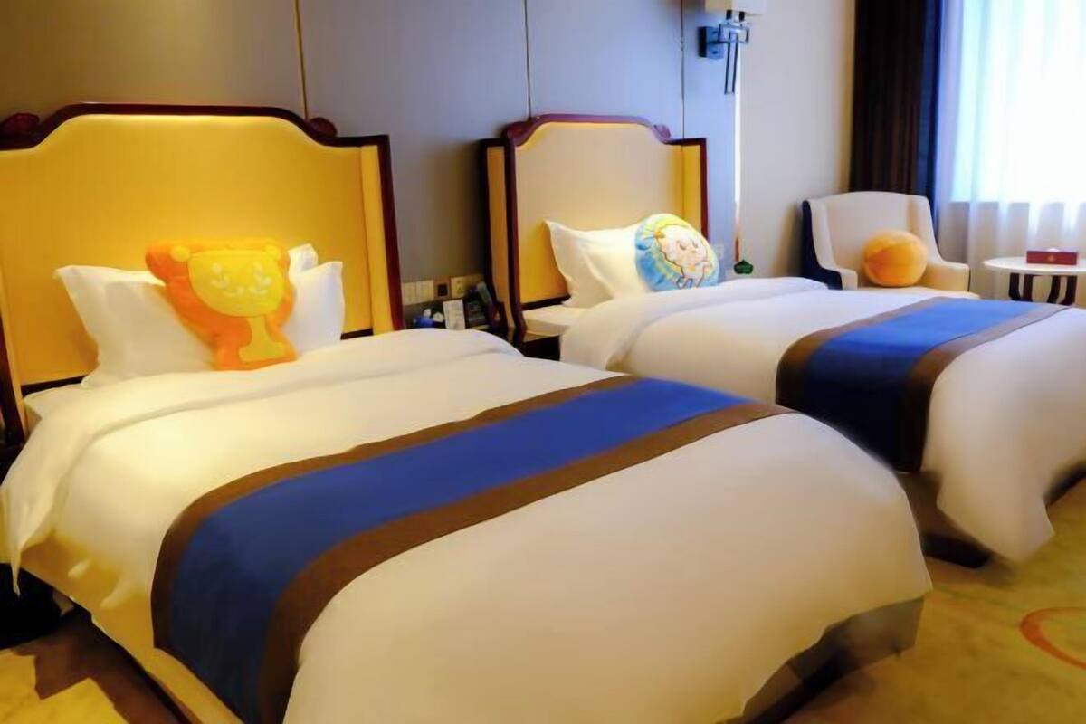 Two double beds with headboards, a small table, a chair, and a window with curtains.