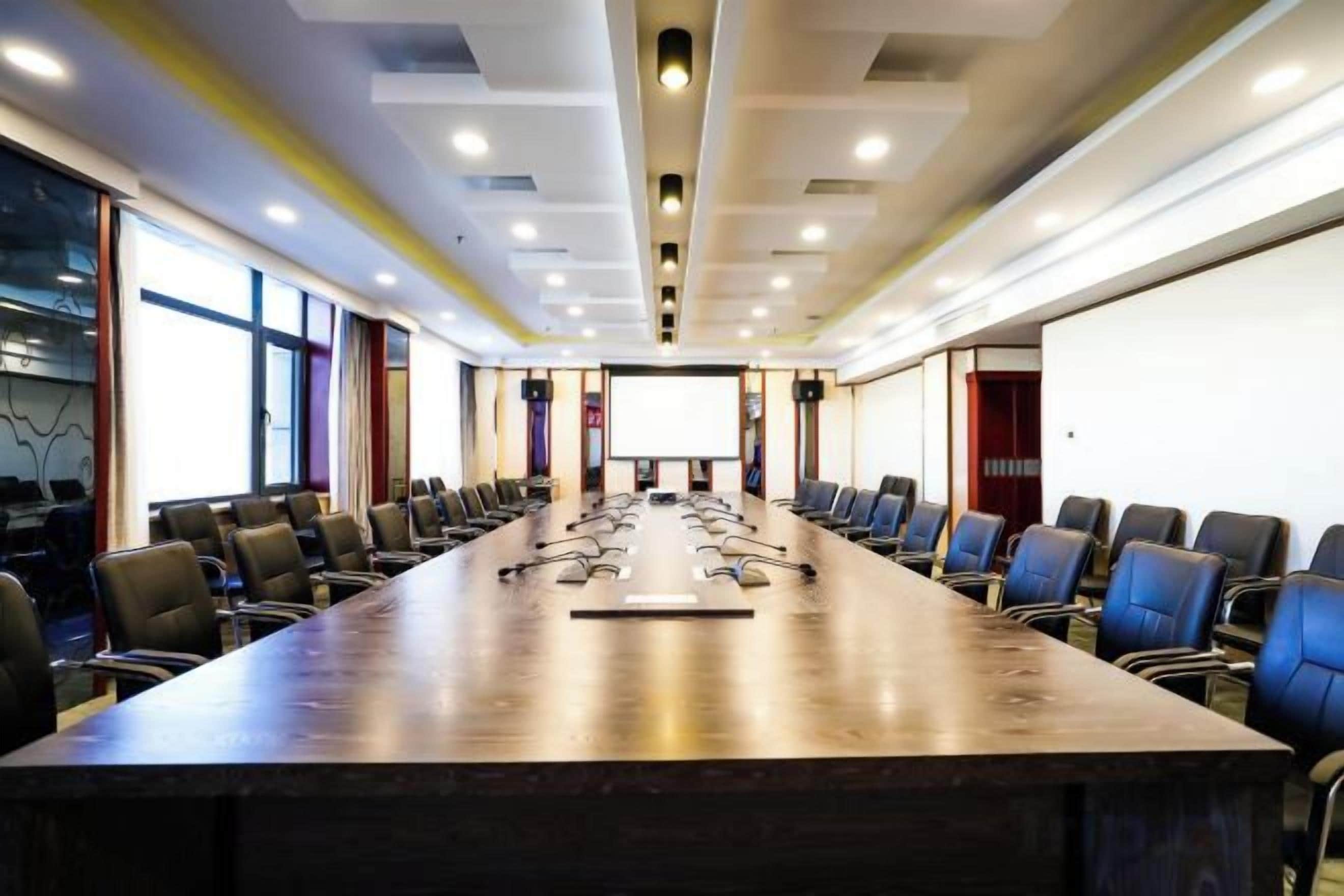 Un salón de conferencias con una larga mesa, sillas, una pantalla de proyector y una pizarra.