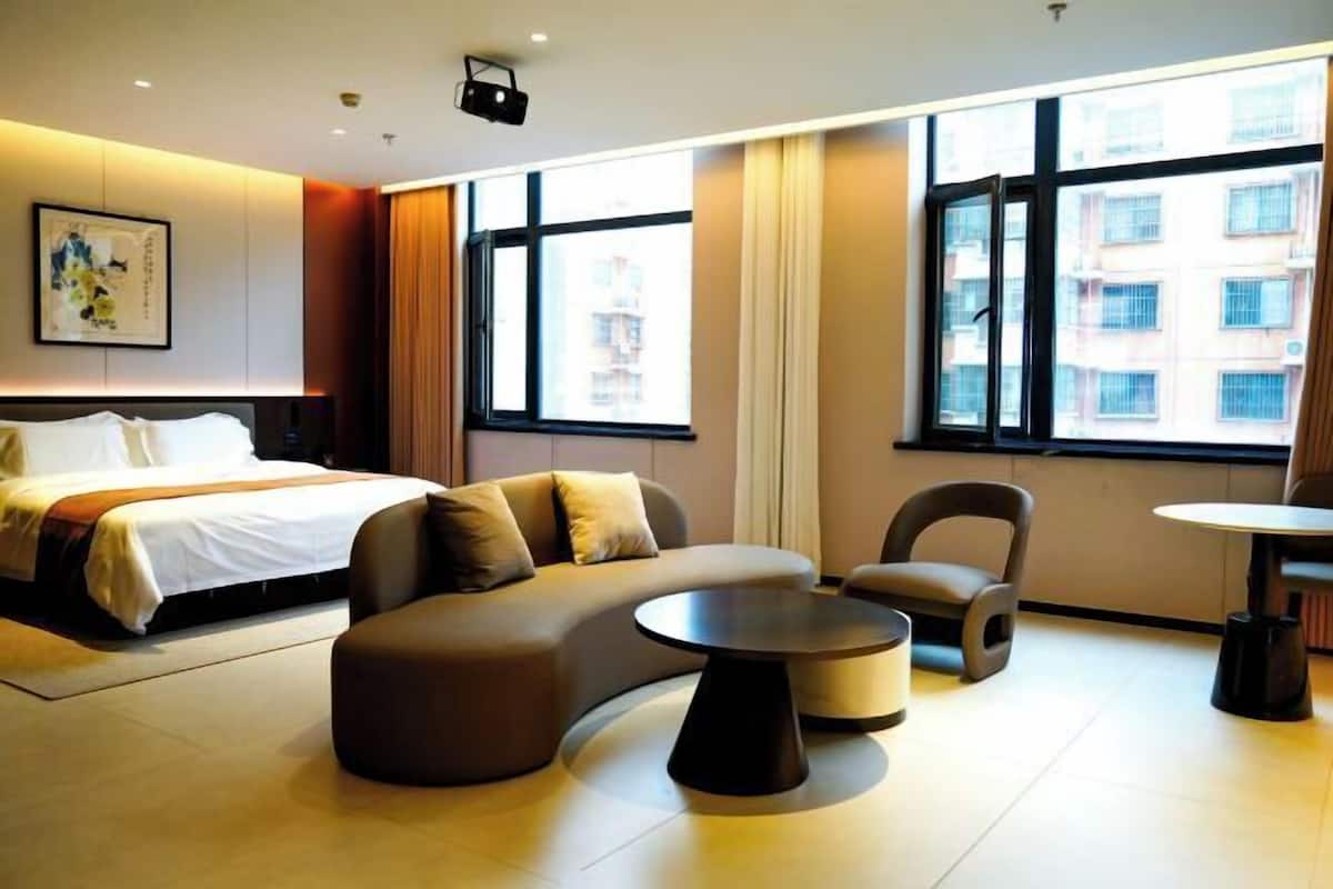 A modern hotel room with a bed, sofa, armchair, and a small table.