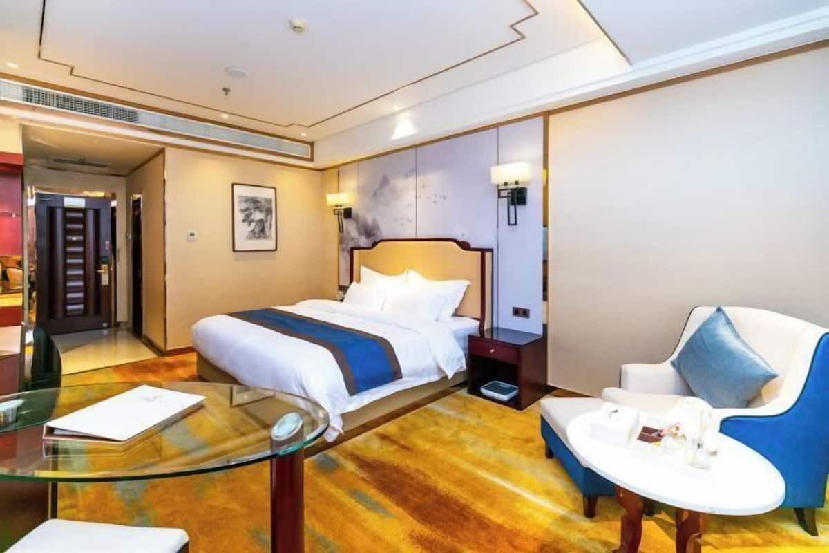 A hotel room with a bed, a glass table, a chair, and a desk.