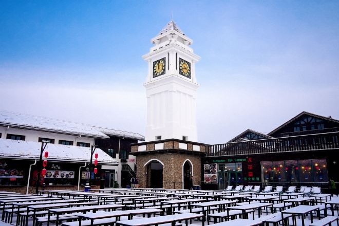 Una torre del reloj, un área con mesas al aire libre y edificios con señalización.