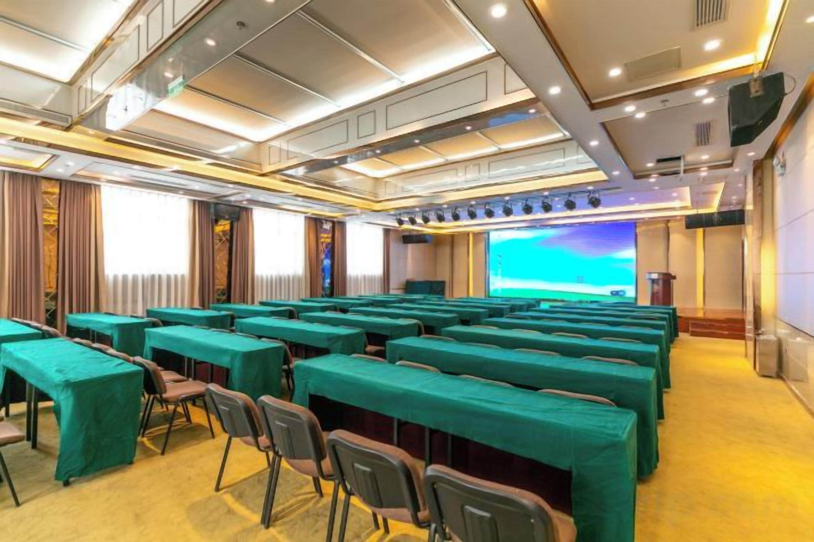 A conference room with rows of tables and chairs, a large screen, and a stage.