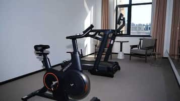 A hotel room with a stationary bike, a treadmill, and a view of the city through large windows.