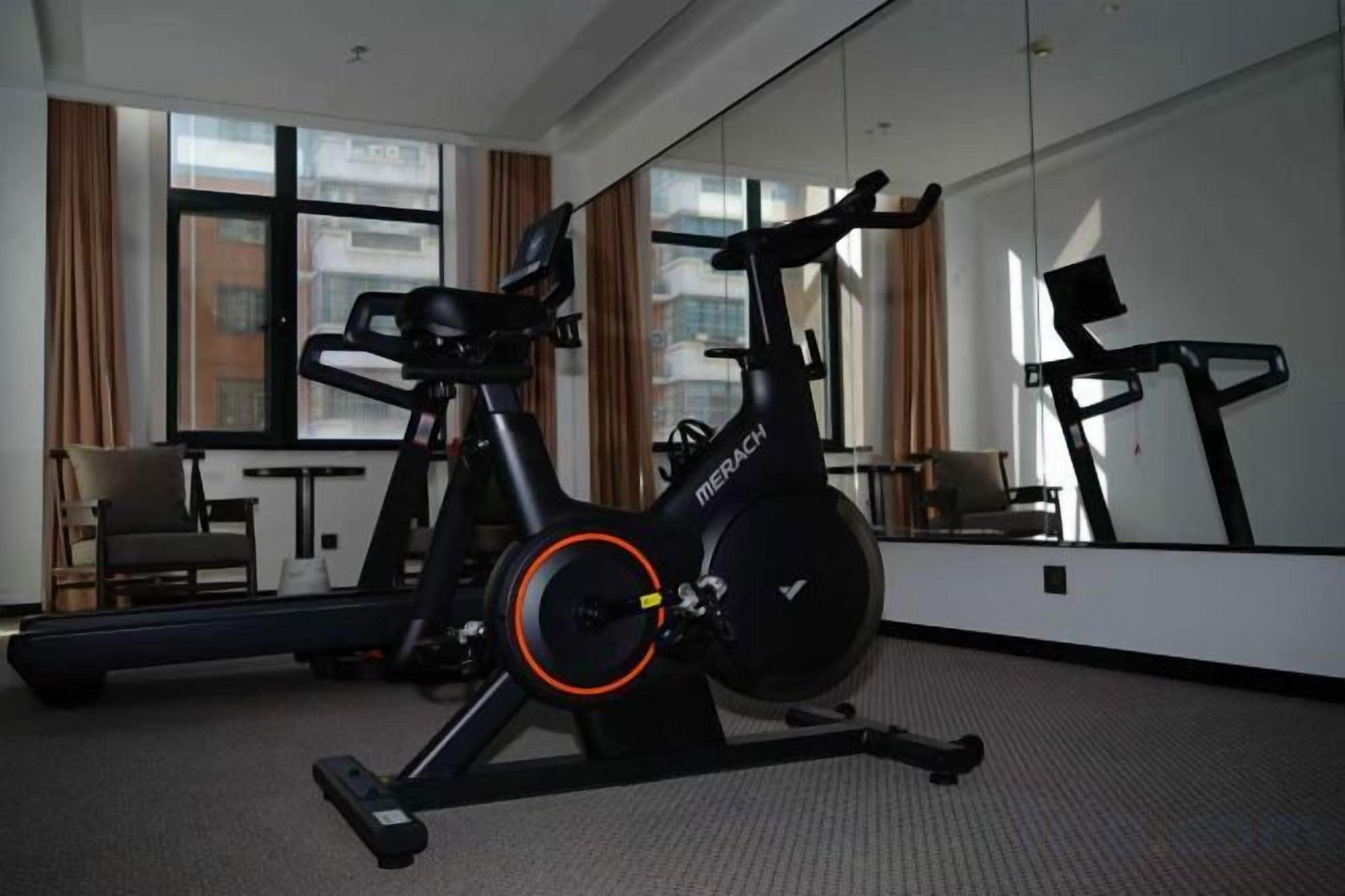 A stationary bike in a hotel room with a large window, a chair, and a table.