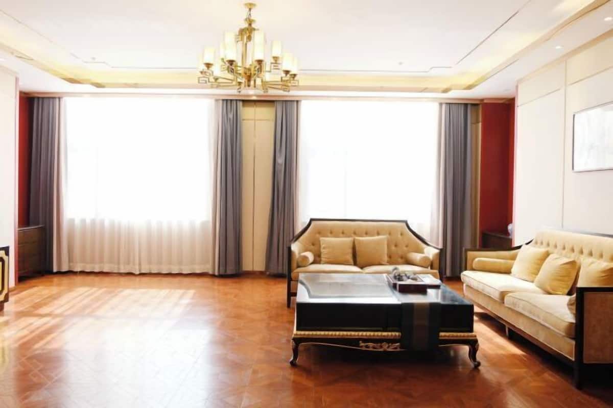 A spacious living room with a large window, a chandelier, and two sofas.