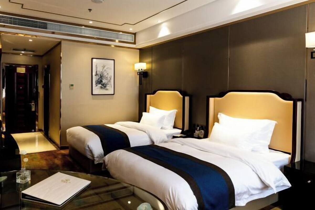 A hotel room with two beds, a desk, a chair, a lamp, and a framed picture on the wall.