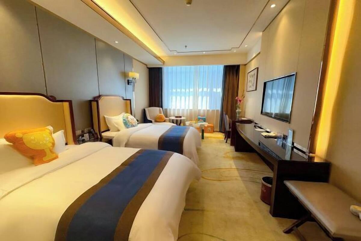 A hotel room with two beds, a desk, a chair, a TV, and a window with curtains.