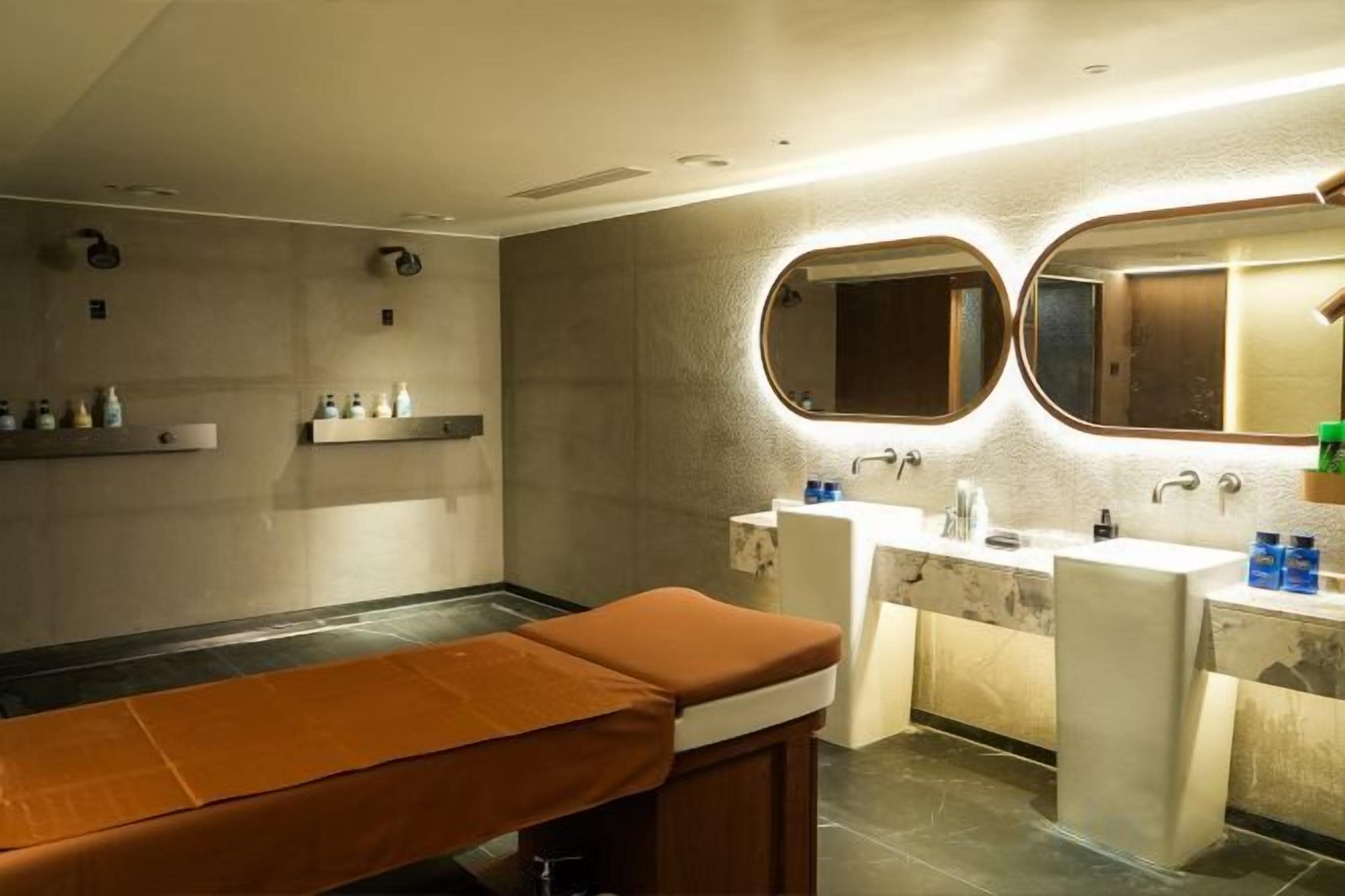 A modern bathroom with a massage table, two sinks, and a large mirror.
