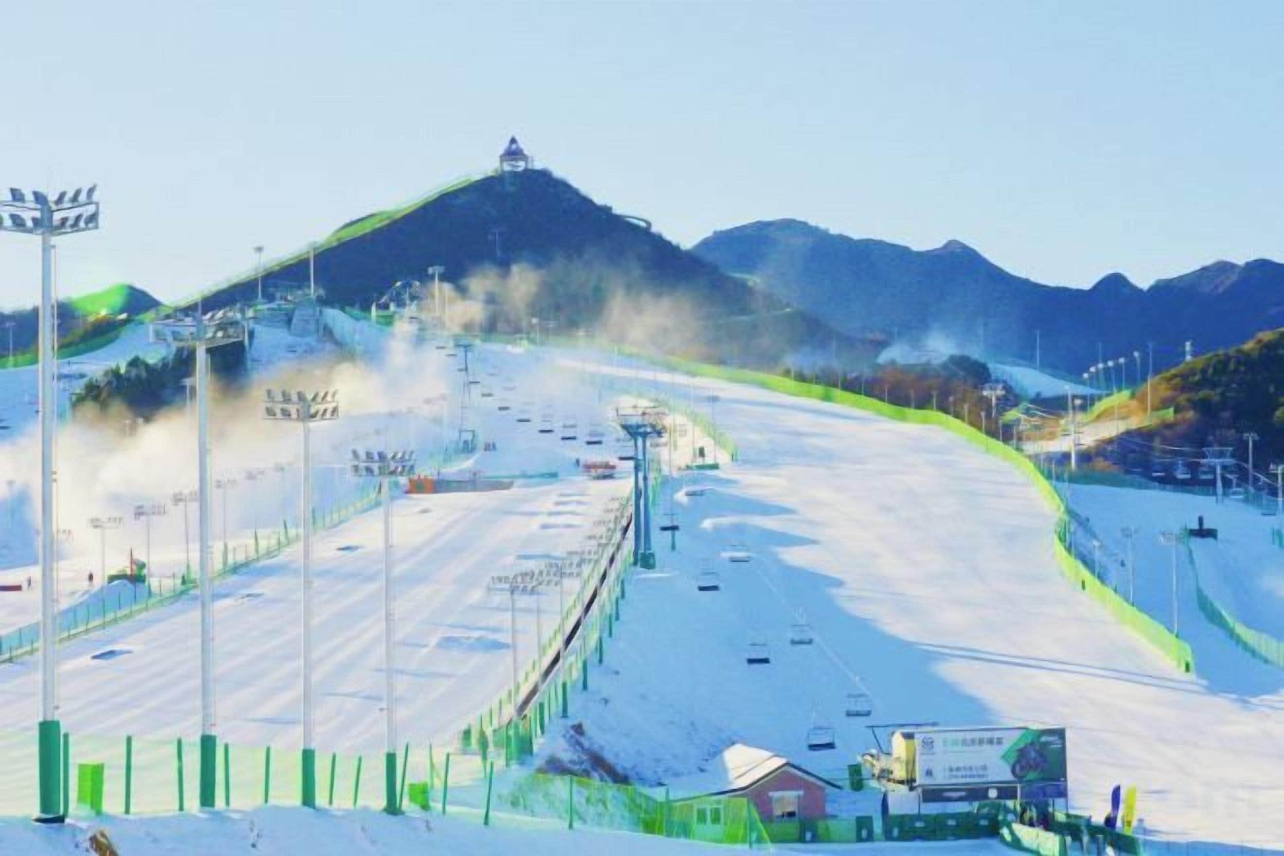 A snow-covered ski slope with a chairlift, a mountain in the background, and a clear sky.