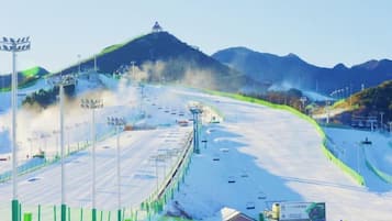 A snow-covered ski slope with a chairlift, a mountain in the background, and a clear sky.