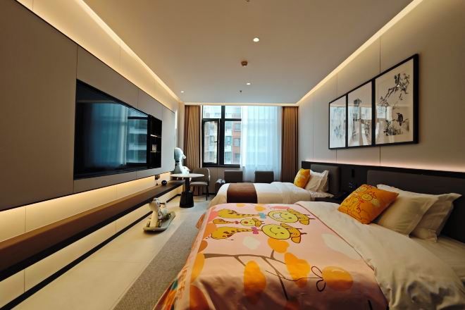 A modern hotel room with a large bed, a flat-screen TV, a desk with a chair, and artwork on the walls.
