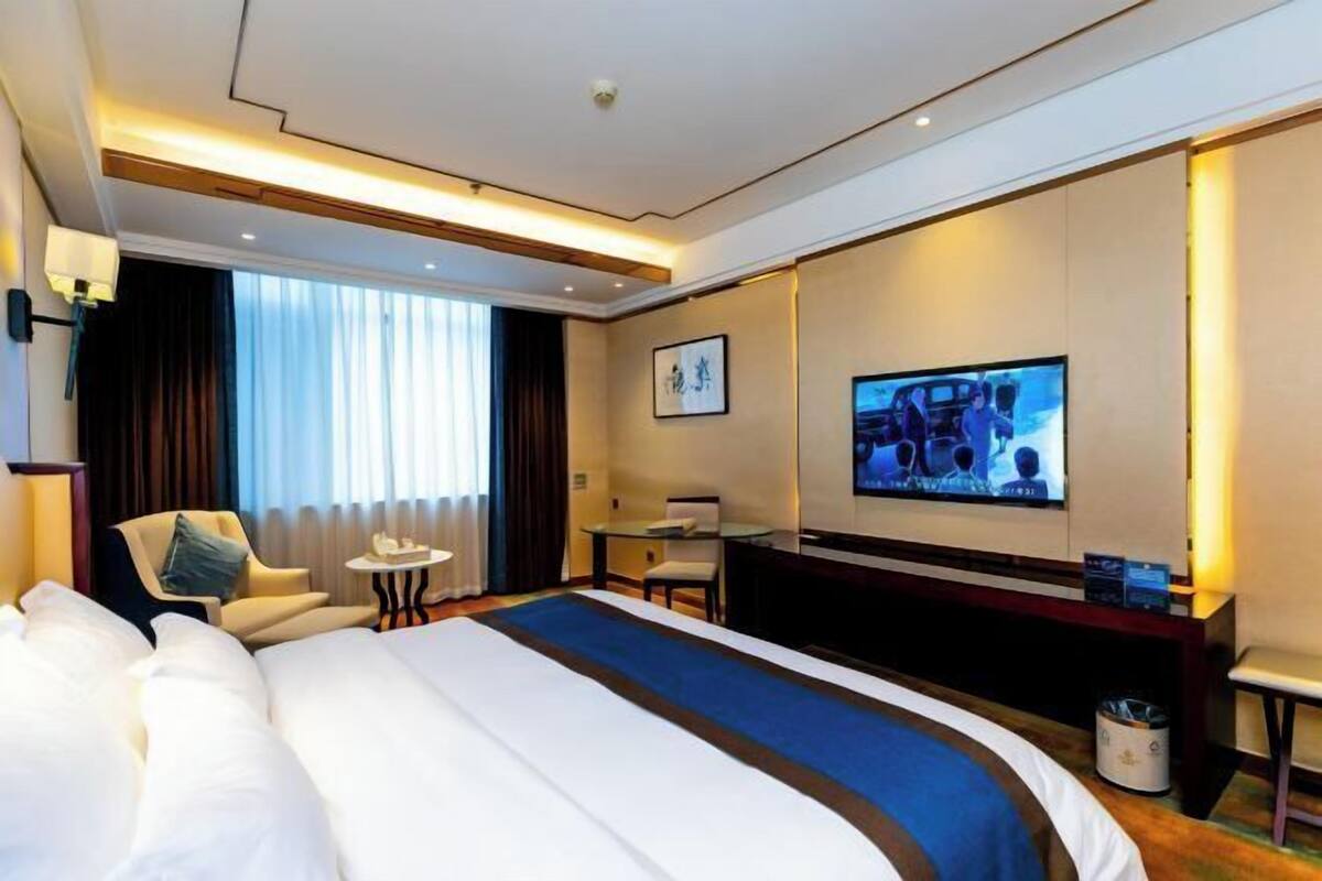 A hotel room with a large bed, a TV, a desk, and a chair.